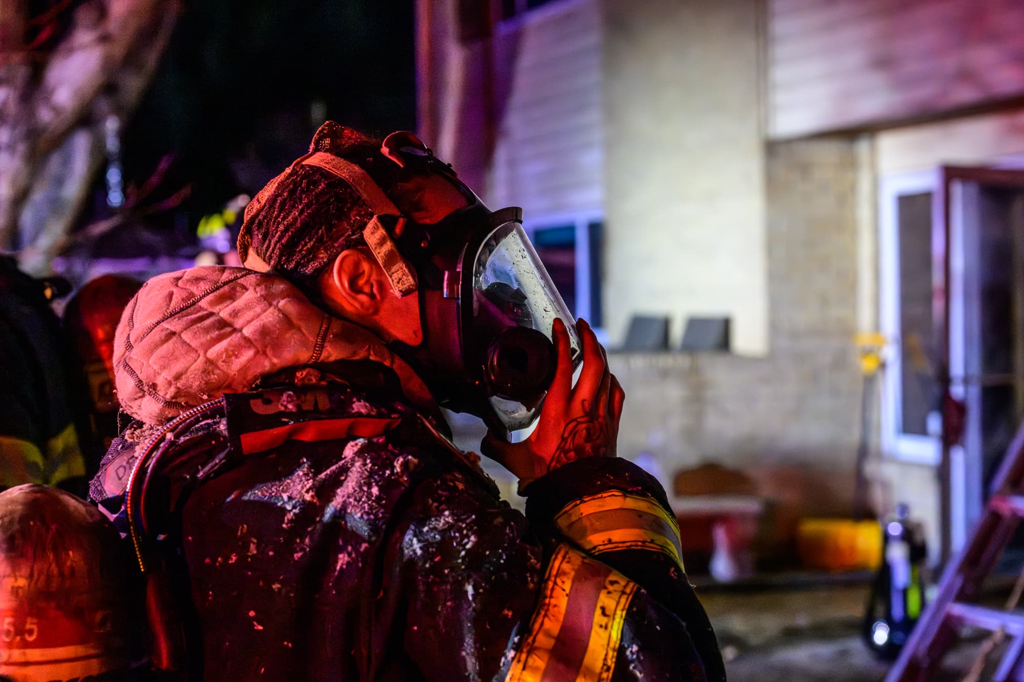 A firefighter covered in debris lifts off her mask at night after working a structure fire