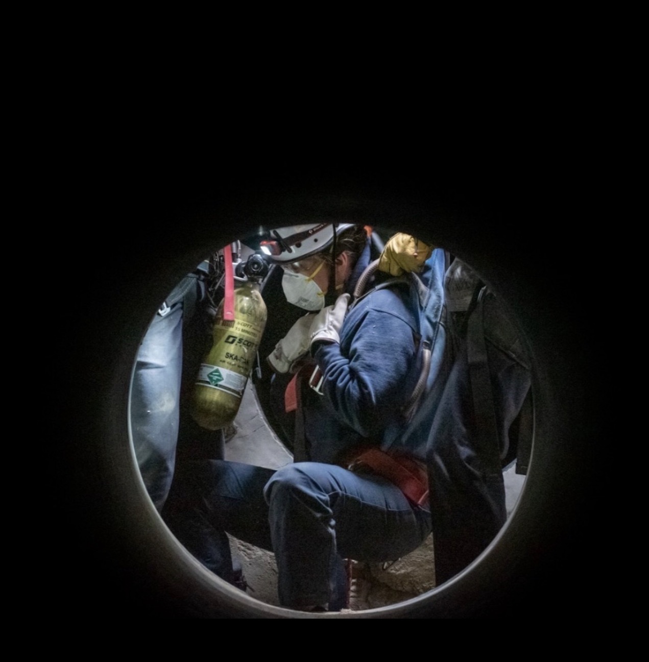 A recruit wearing a respirator and headlamp works through a confined-space training tunnel